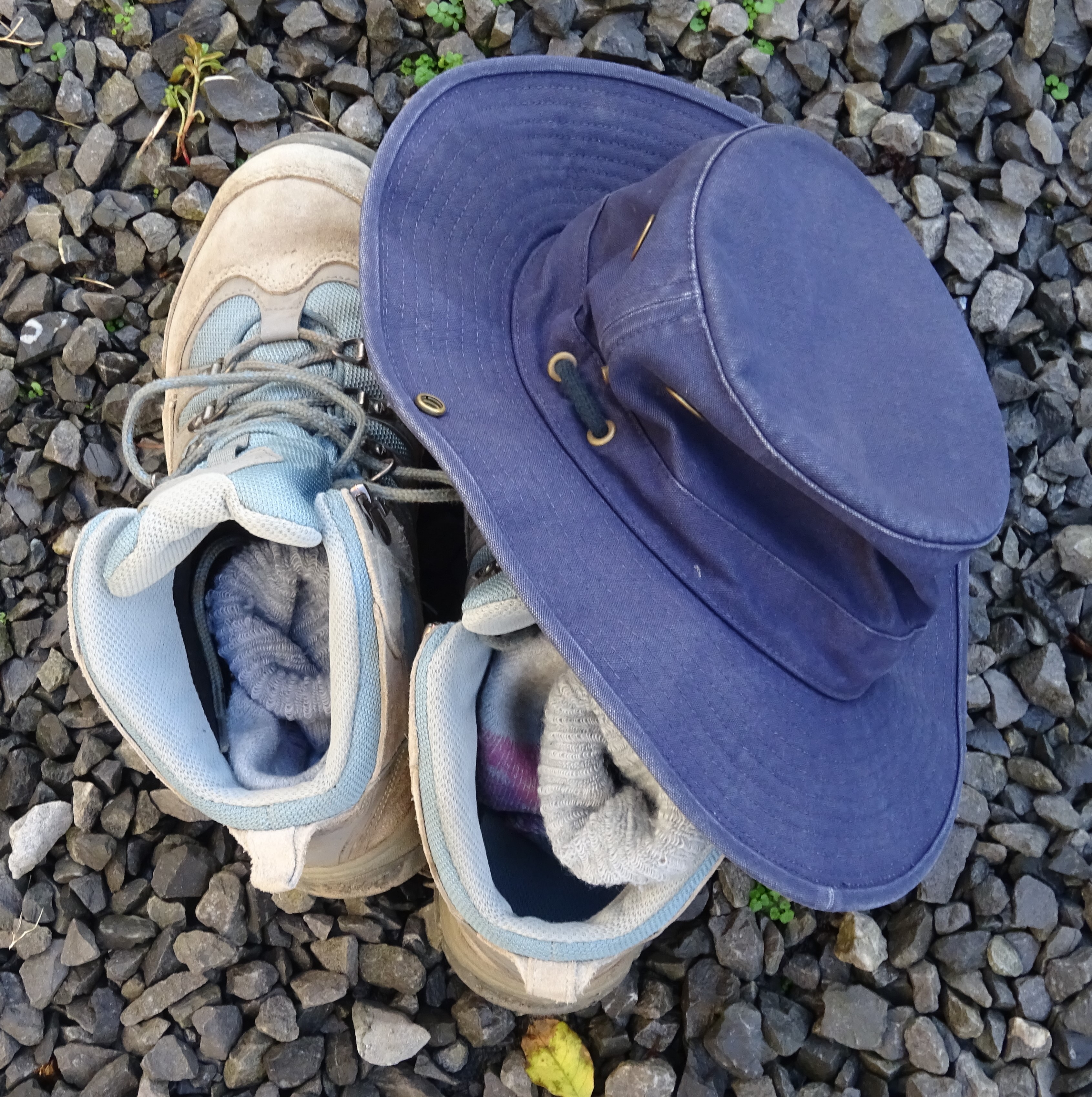 A pair of worn walking boots and an old, blue, wide brimmed hat. 